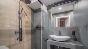 A modern bathroom with a glass shower enclosure, a large white sink, and a mirror above the sink.