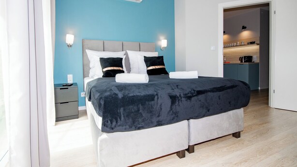 A modern bedroom with a grey upholstered bed, white pillows, and a blue accent wall.