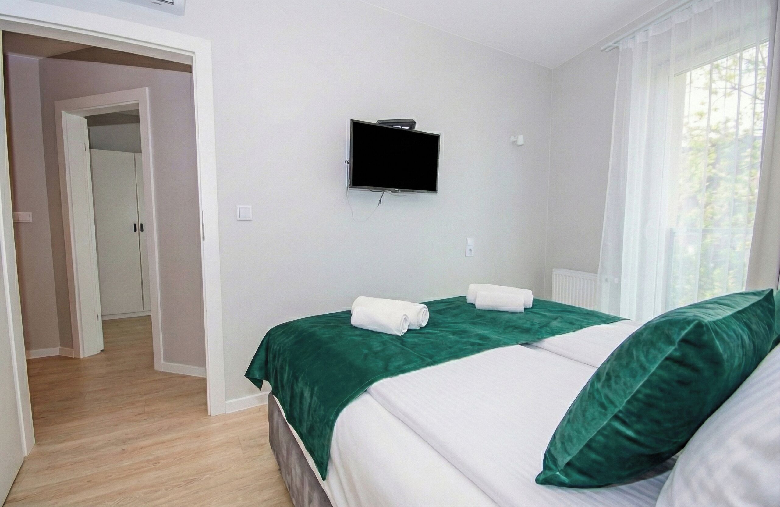 A hotel room with a bed, a TV mounted on the wall, and a window with curtains.