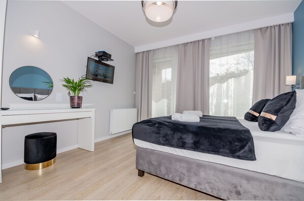 Quarto moderno com cama, mesa de cabeceira e uma janela grande com cortinas.