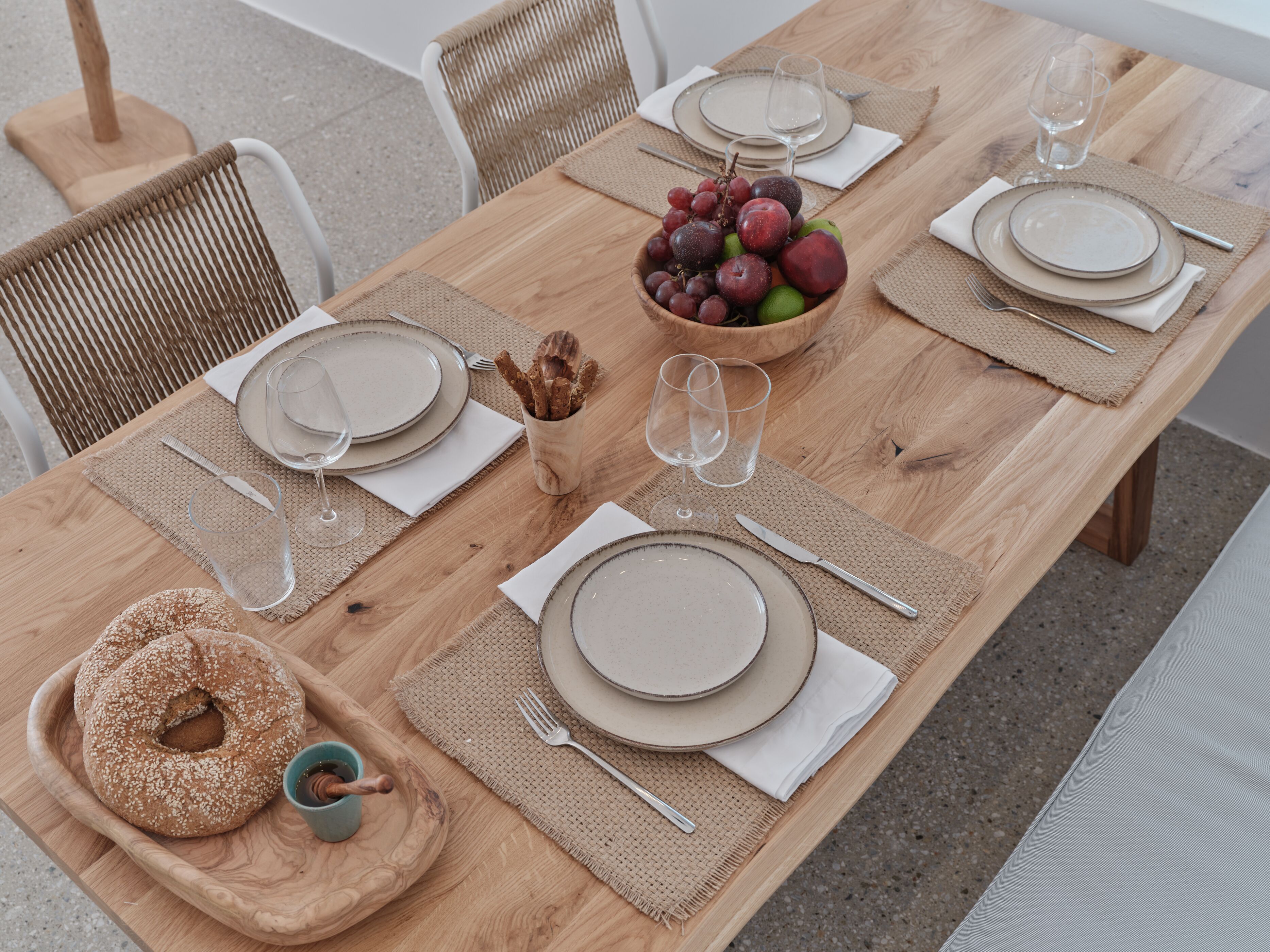 A wooden dining table set with plates, glasses, and a bowl of fruit.
