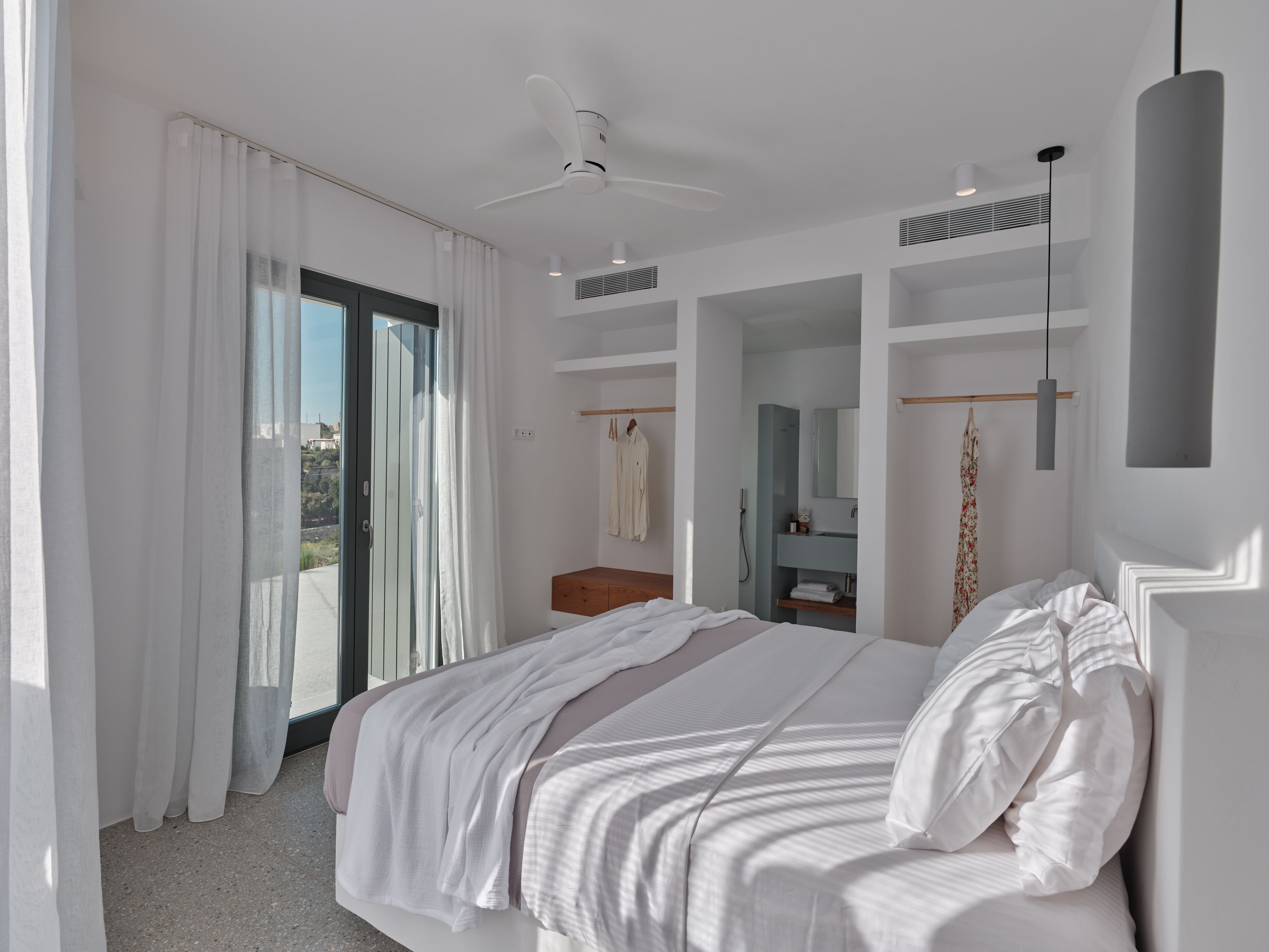 A modern bedroom with a large bed, a ceiling fan, a walk-in closet, and a bathroom with a shower and mirror.