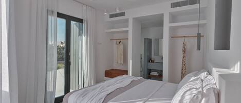 A modern bedroom with a large bed, a ceiling fan, a walk-in closet, and a bathroom with a shower and mirror.