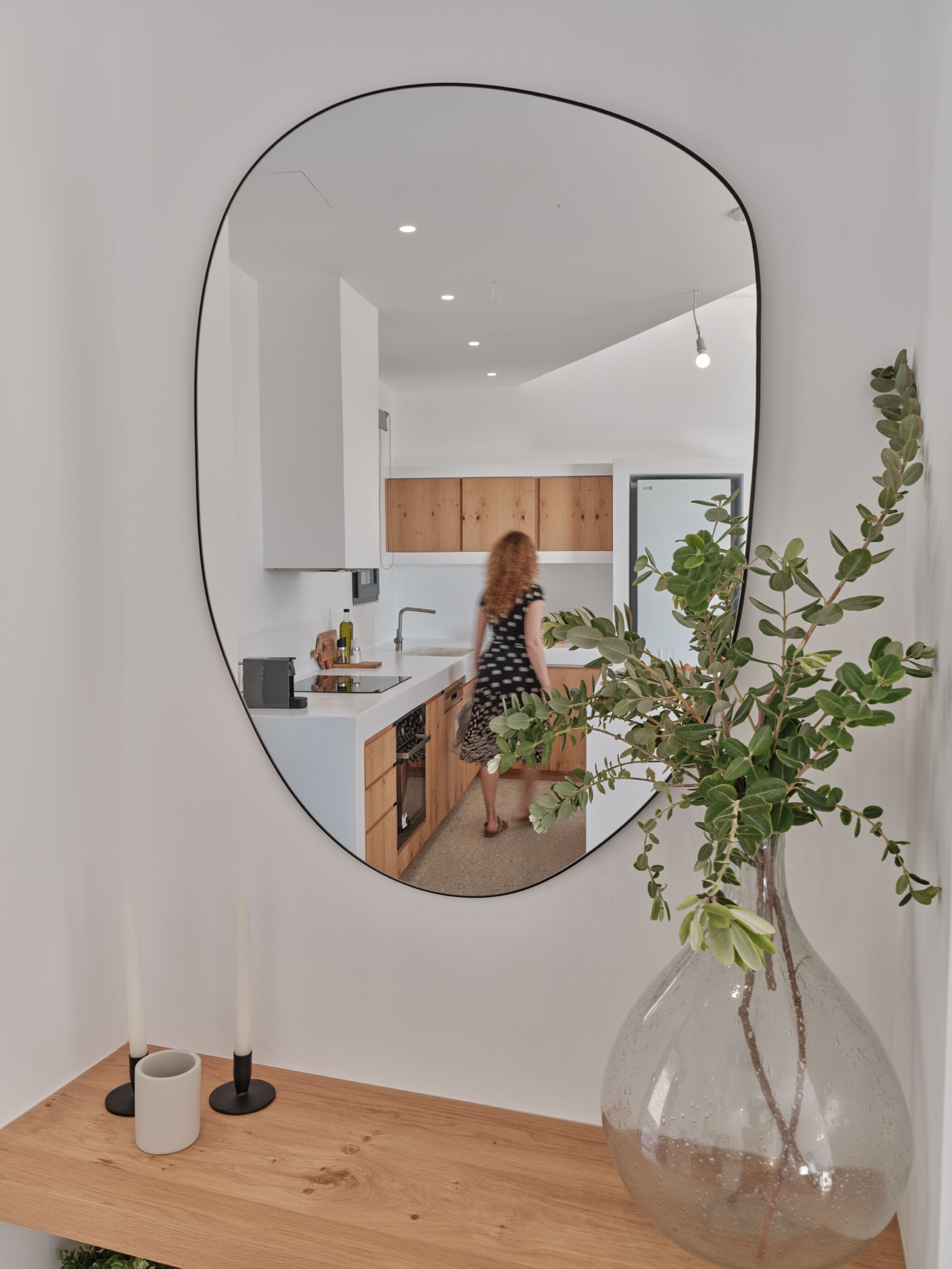 Una cocina moderna con armarios de madera, encimera blanca y un espejo ovalado grande en la pared.