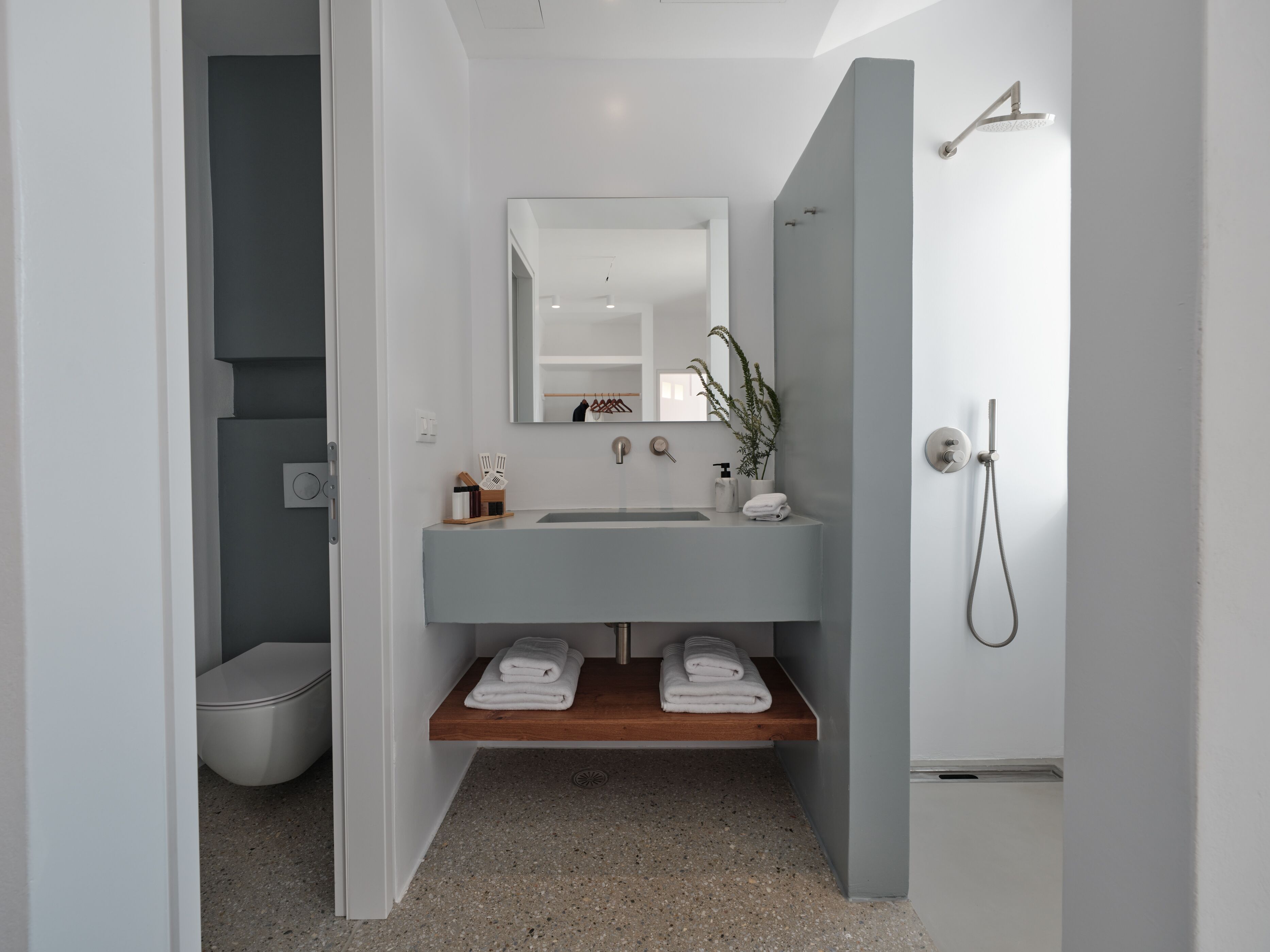 A modern bathroom with a grey sink, a mirror, a shower, and a toilet.