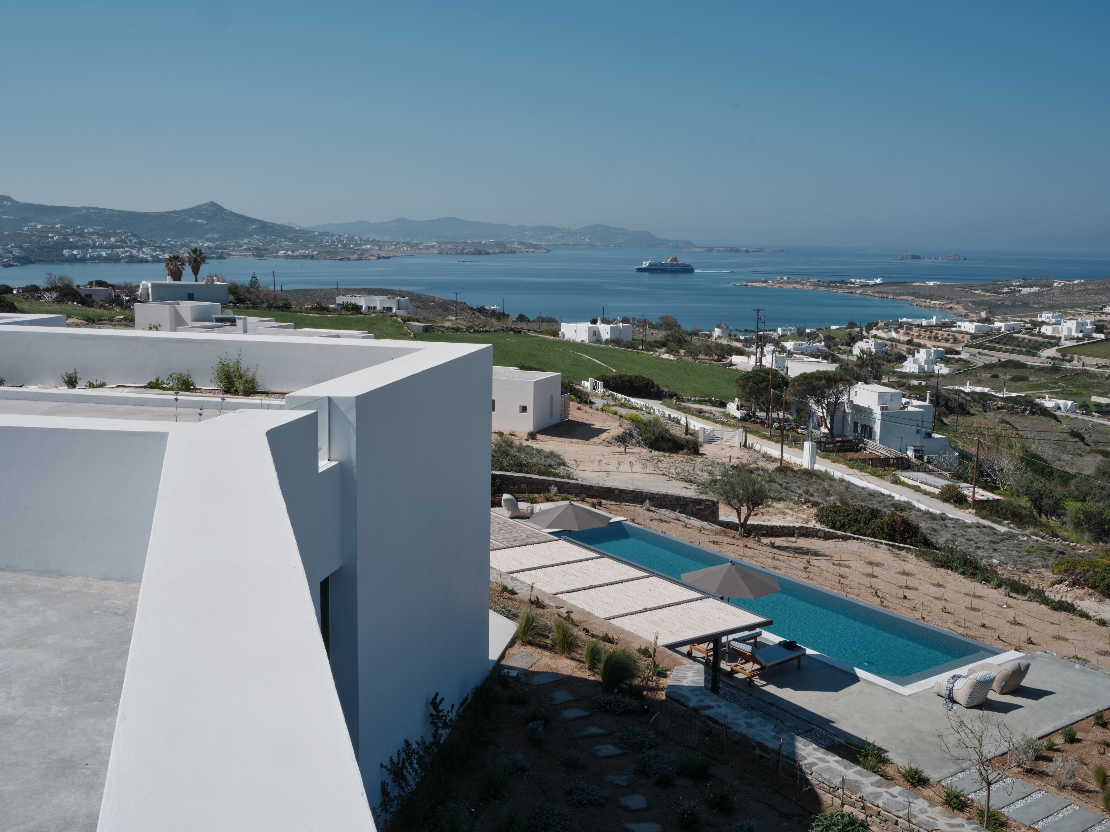 Una villa moderna con piscina en la azotea, arquitectura blanca y vistas al mar y montañas distantes.