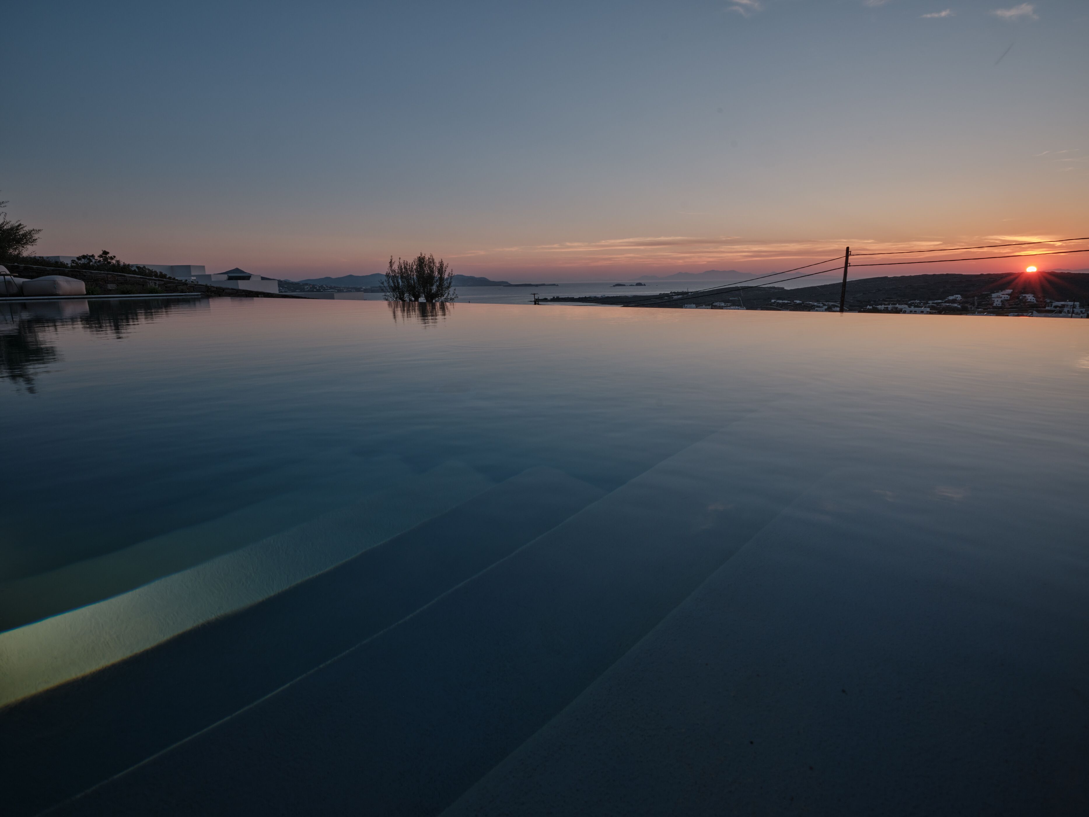 A serene infinity pool with a clear view of the sunset over the water.