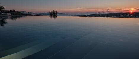 A serene infinity pool with a clear view of the sunset over the water.