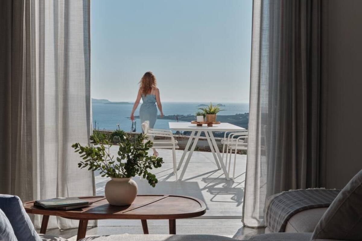Una habitación con vista al mar, un comedor con mesa y sillas, y una planta en maceta sobre una mesa de centro.