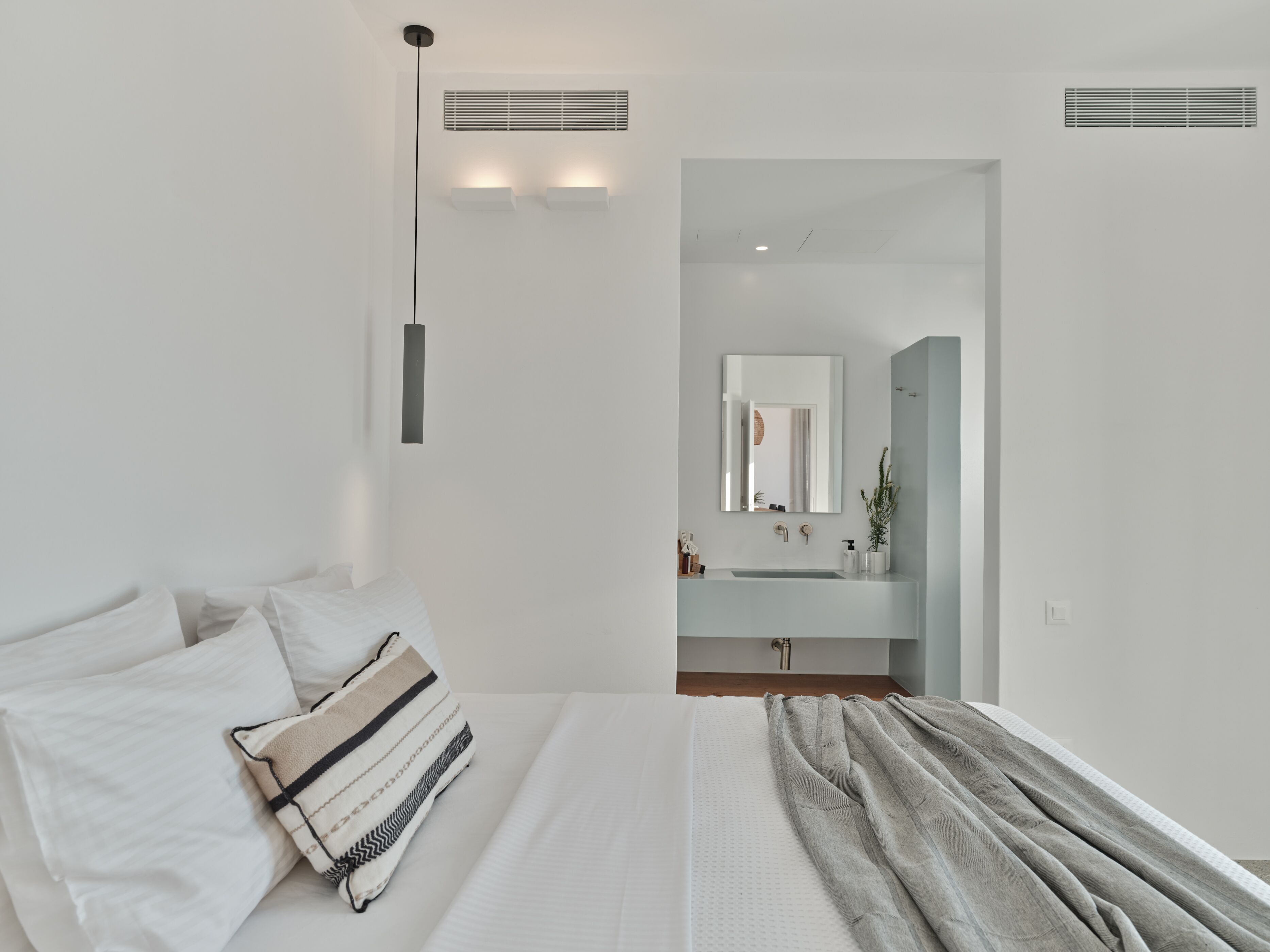 Een moderne slaapkamer met een bed, kussens, een nachtkastje en een groot raam.