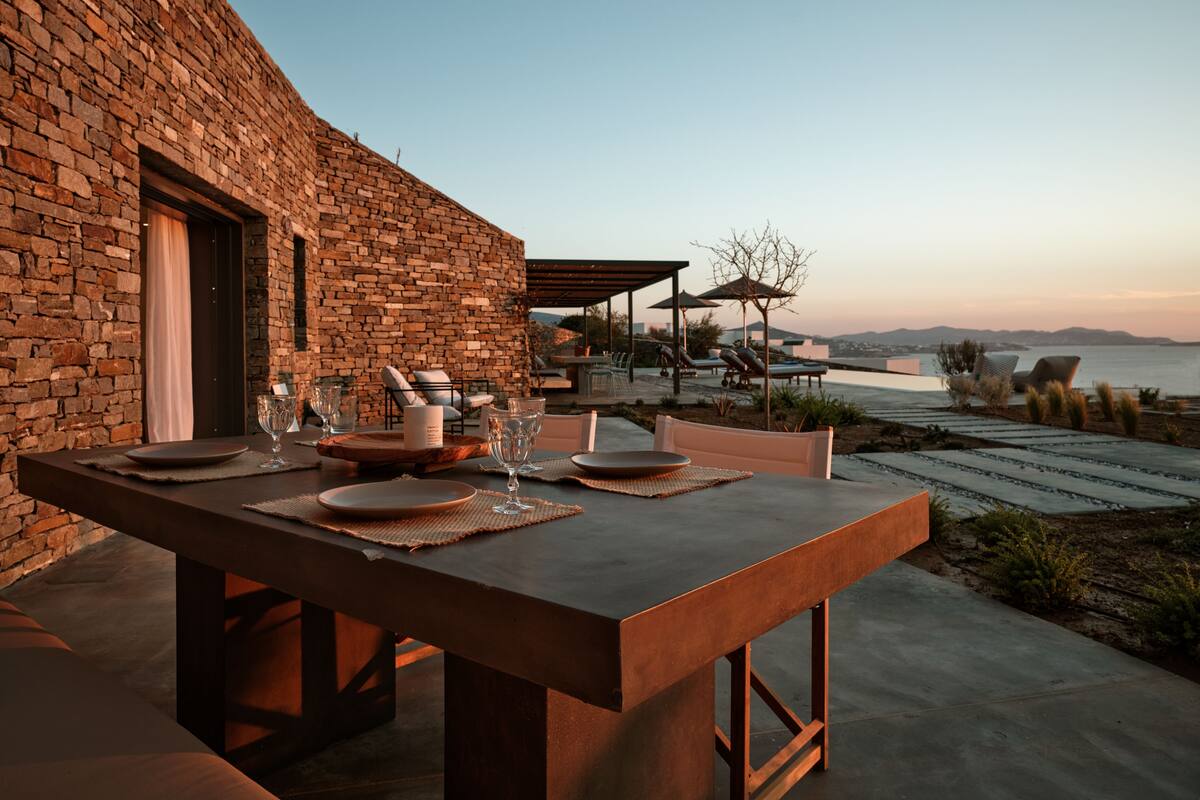 Un comedor con una mesa para dos, una pared de piedra y vista al mar.