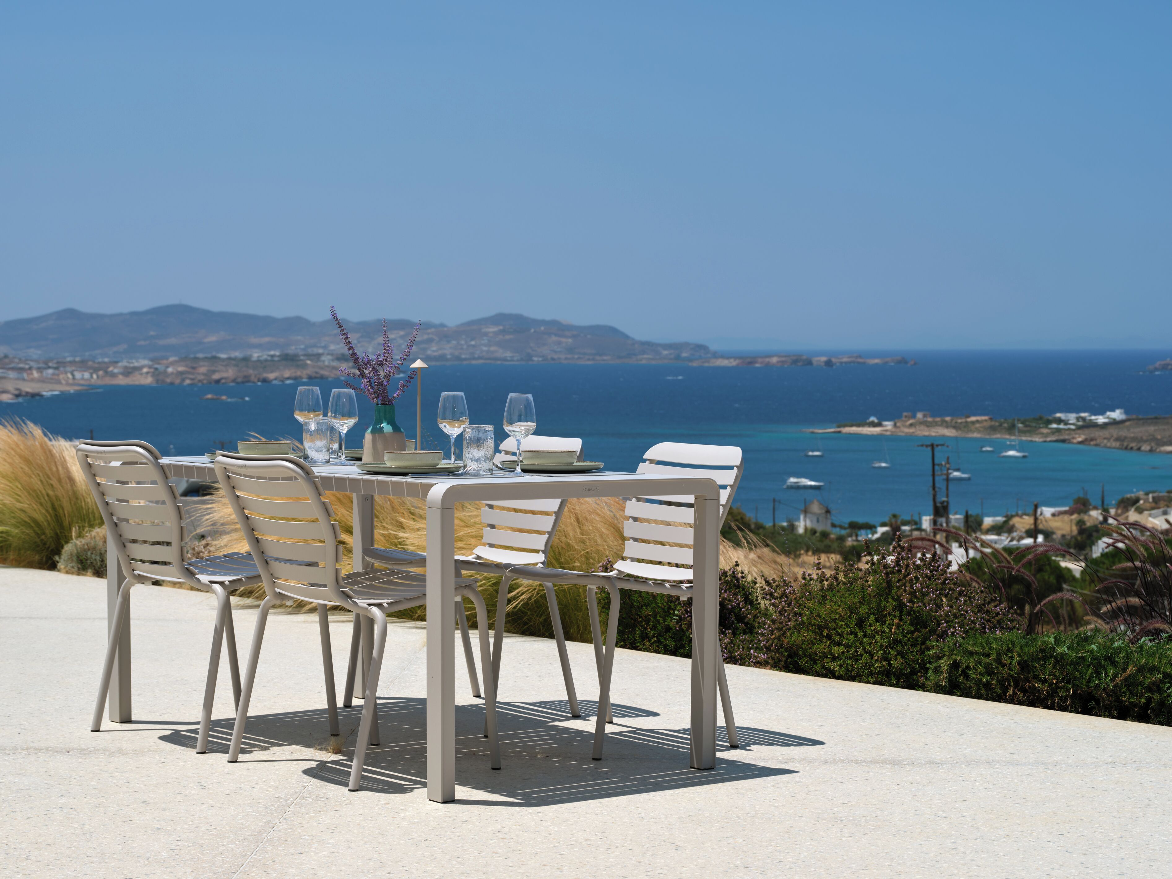 Une table dressée pour quatre personnes, avec vue sur la mer et les montagnes en arrière-plan.