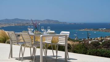 Une table dressée pour quatre personnes, avec vue sur la mer et les montagnes en arrière-plan.