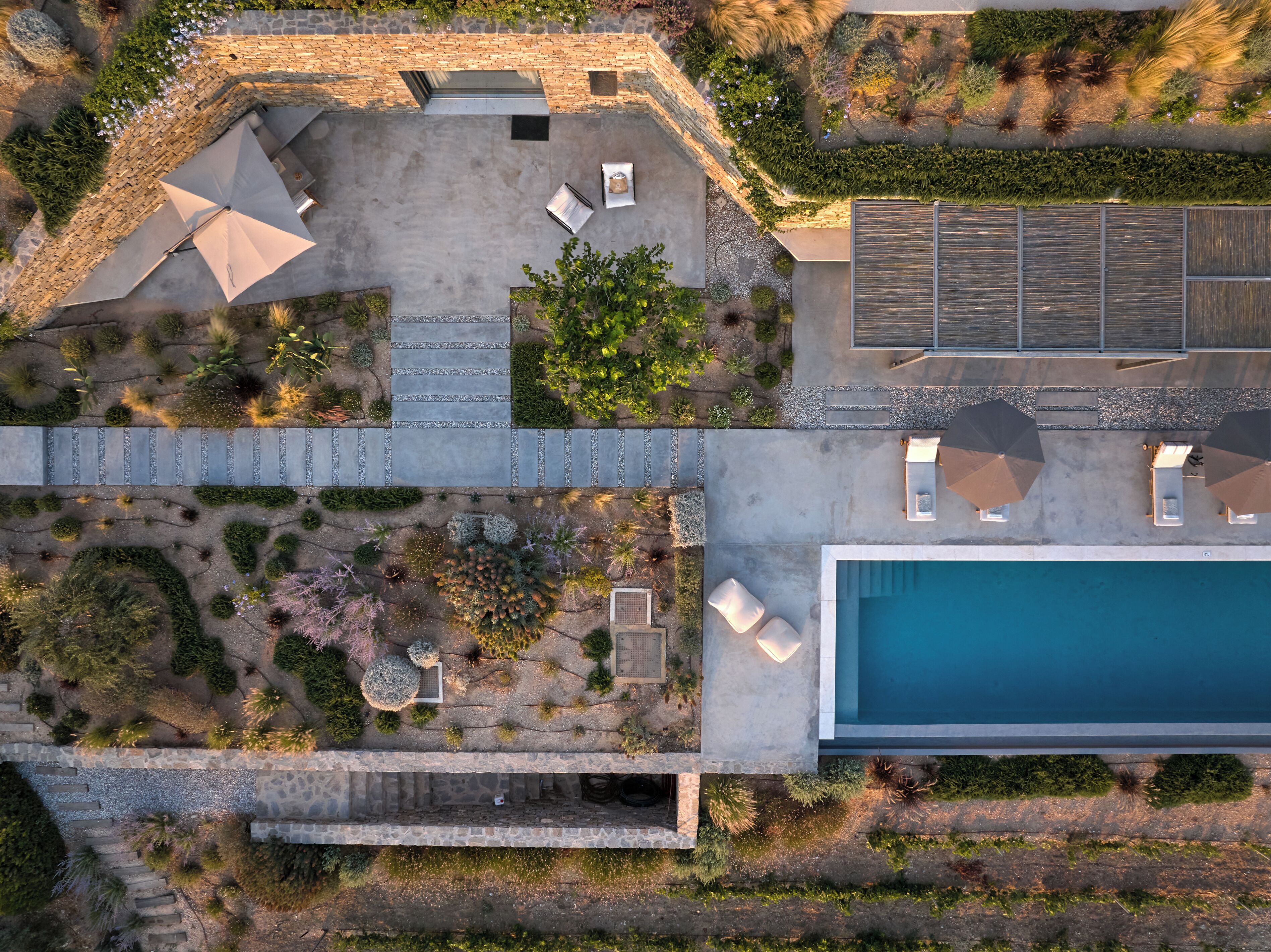 An aerial view of a modern property with a swimming pool, outdoor seating, and a garden area.