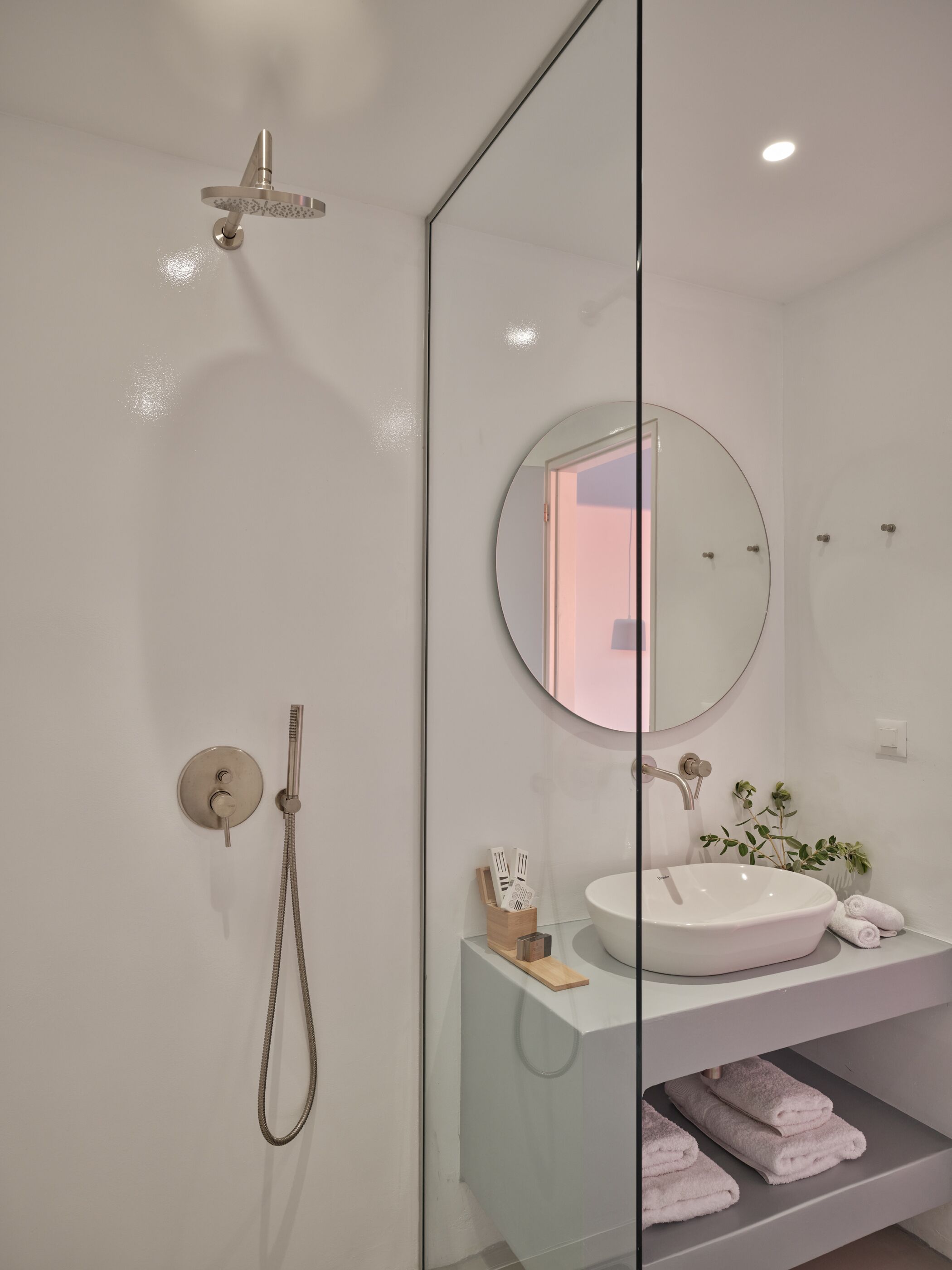 Un bagno moderno con box doccia in vetro, uno specchio rotondo, un lavandino bianco e asciugamani piegati con cura.