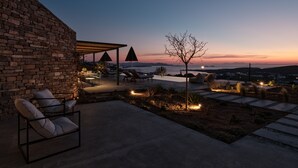 A patio with outdoor seating, a pool, and a view of the sea at dusk. - Olithos Villas (Paros)