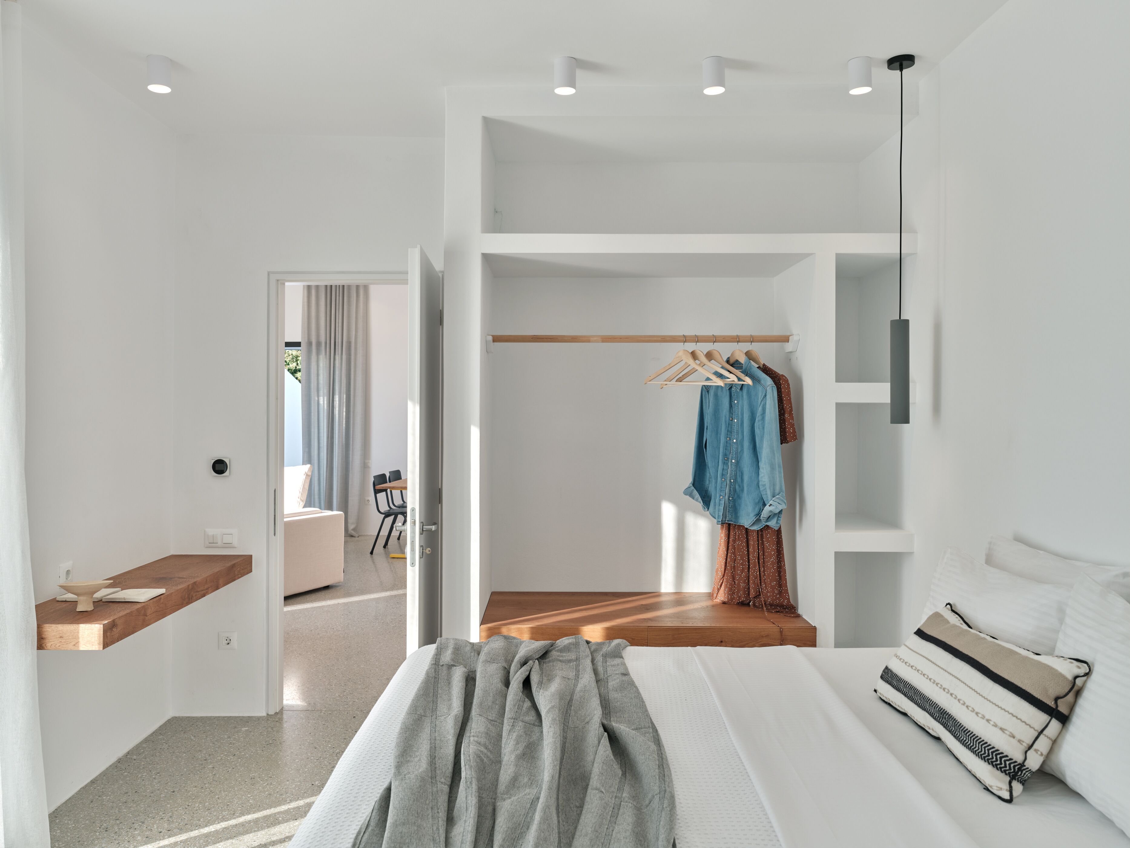 A modern bedroom with a bed, a wooden bedside table, a hanging wardrobe, and a view of the outside.