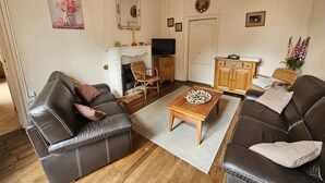A living room with two leather sofas, a wooden coffee table, a fireplace, a television, and a mirror. - Gîte Du Theil Au Servant (LA CHAPELLE-VIVIERS)