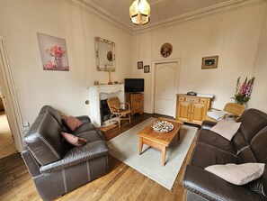 A living room with two leather sofas, a wooden coffee table, a fireplace, a television, and a mirror.