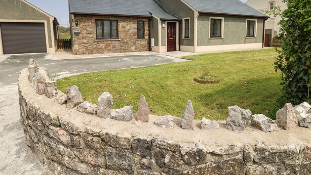 Una casa de dos pisos con fachada de piedra y techo gris, rodeada por un muro de piedra y un césped.