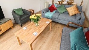 Una sala de estar con un sofá gris, una mesa de centro de madera, un sillón gris y un televisor sobre un mueble de madera.