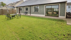 Una casa moderna con un amplio ventanal corredero, patio trasero cercado y un porche con mobiliario exterior.
