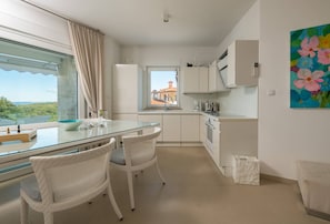 A modern kitchen with white cabinets, a glass dining table, wicker chairs, and a view of a coastal landscape. - Dream Lounge With sea View (Pula)