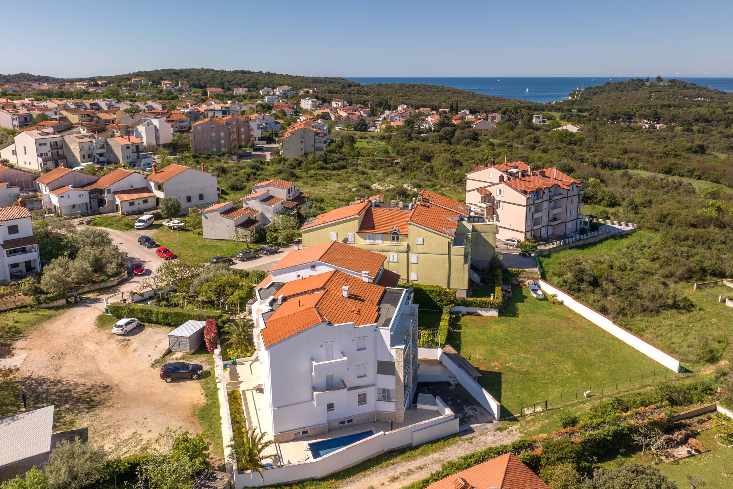 A residential area with multiple buildings, a swimming pool, and a view of the sea.