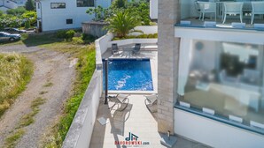 Ett modernt hus med en swimmingpool, en uteplats med stolar och utsikt över de omkringliggande husen.