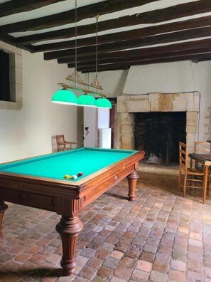 A pool table with balls, a fireplace, and a dining area with chairs.