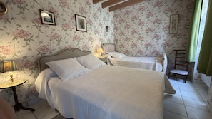 Ein Schlafzimmer mit zwei Betten, blumigem Wandpapier, einem Nachttisch mit Lampe und einem Sessel.