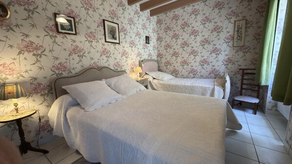 Ein Schlafzimmer mit zwei Betten, blumigem Wandpapier, einem Nachttisch mit Lampe und einem Sessel.
