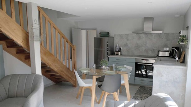 Eine moderne Küche mit Essbereich, einer Holztreppe und grauen Sitzmöbeln.