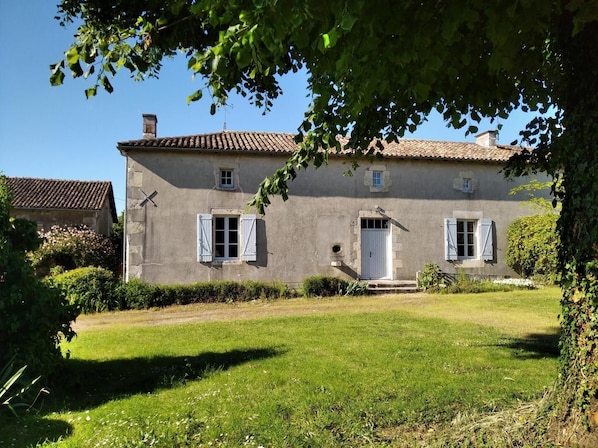 Une maison Ă deux Ă©tages, avec un toit recouvert de tuiles, une porte dâentrĂ©e et deux fenĂȘtres dotĂ©es de volets.