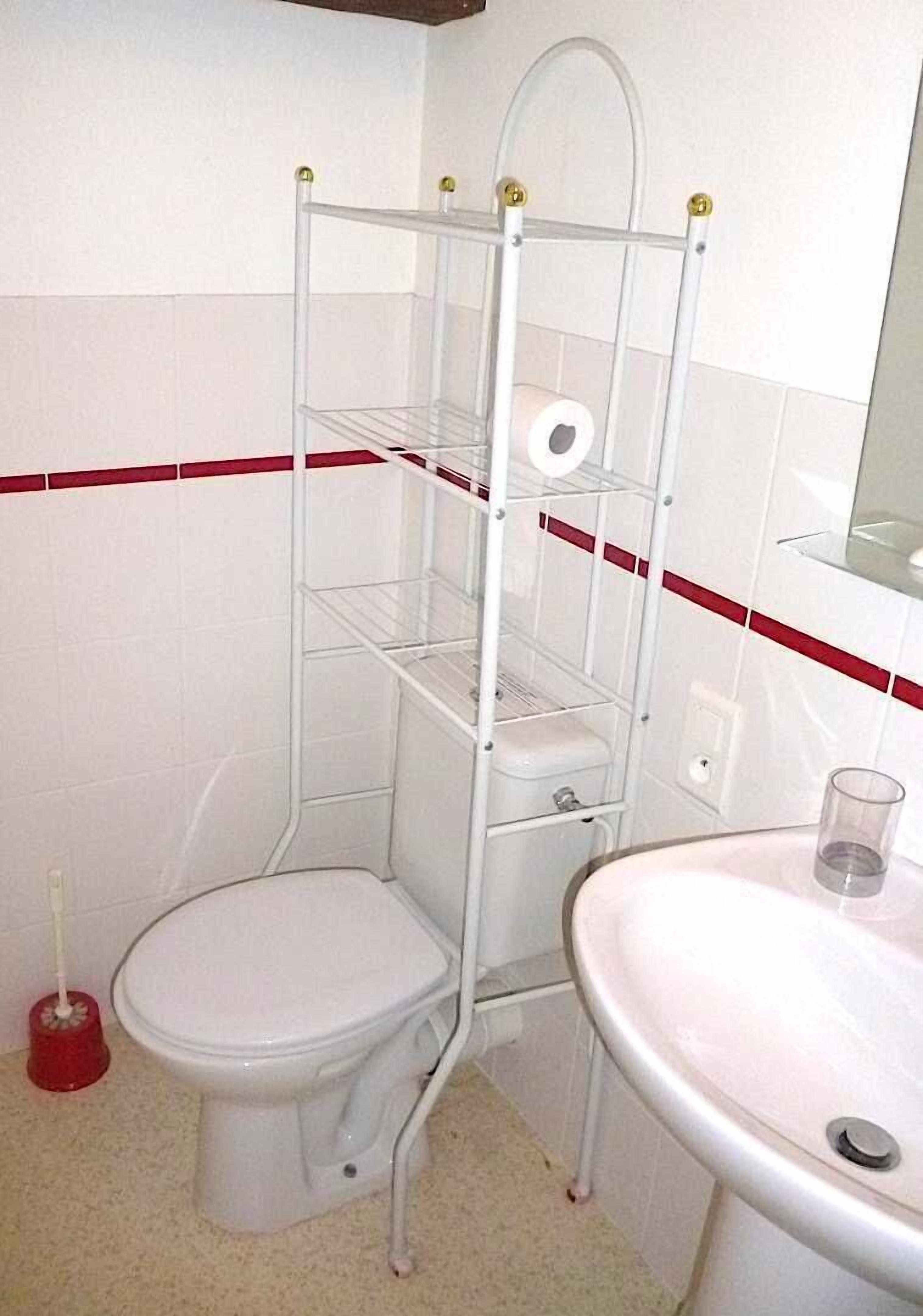 A corner bathroom with a toilet, a white sink, and a metal shelf unit with a toilet paper holder.