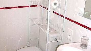A corner bathroom with a toilet, a white sink, and a metal shelf unit with a toilet paper holder.