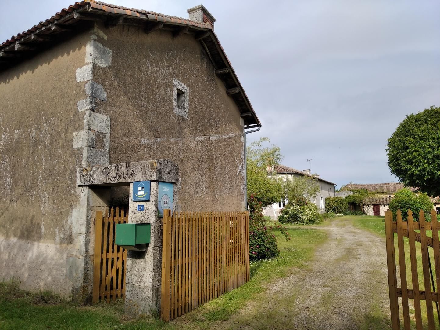 Un edificio rustico con facciata vissuta, un cancello in legno e un vialetto stretto che vi conduce.