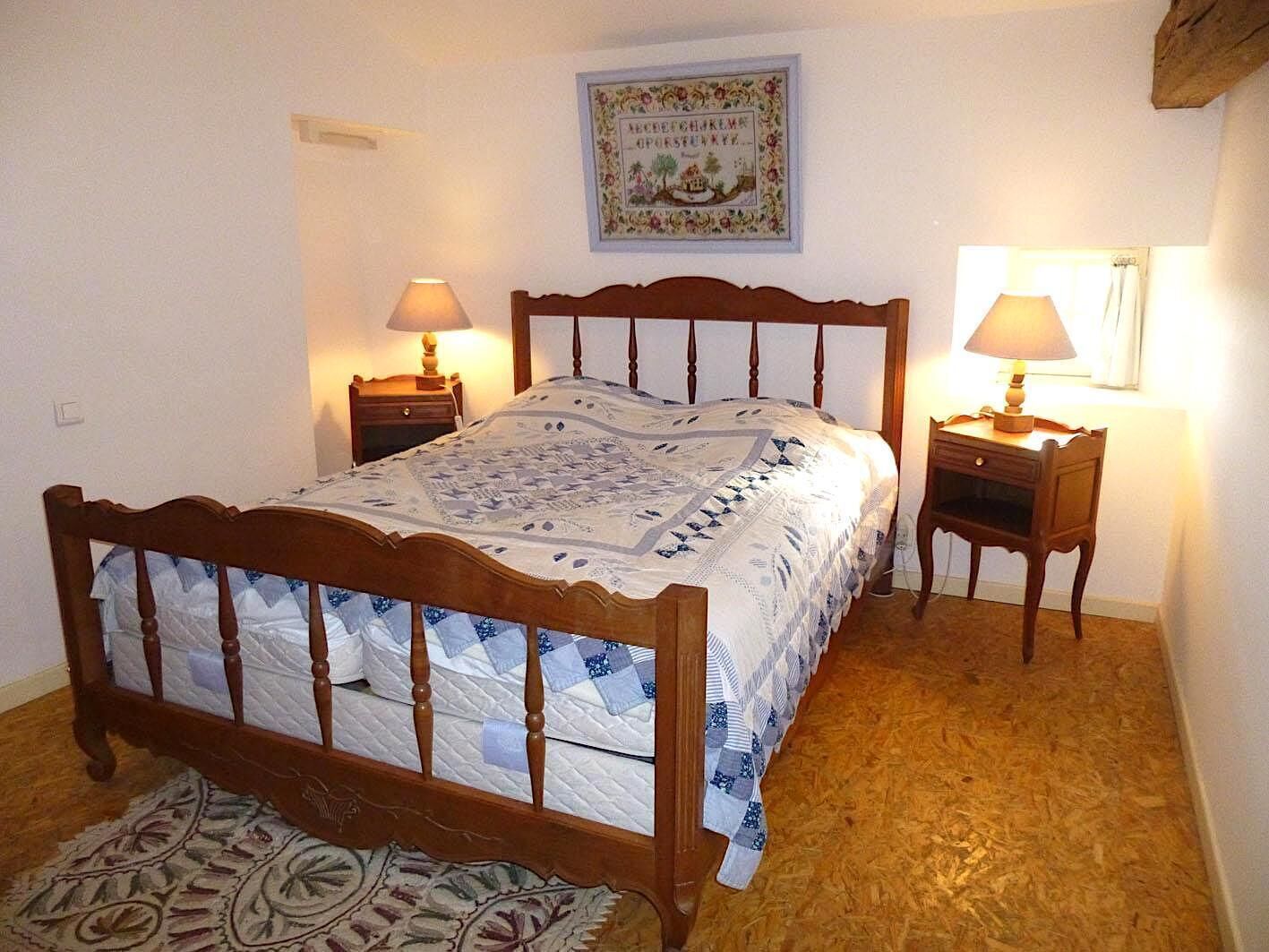 Ein Schlafzimmer mit einem hölzernen Bett, zwei Nachttischen mit Lampen, einem gemusterten Teppich und einem gerahmten Bild an der Wand.