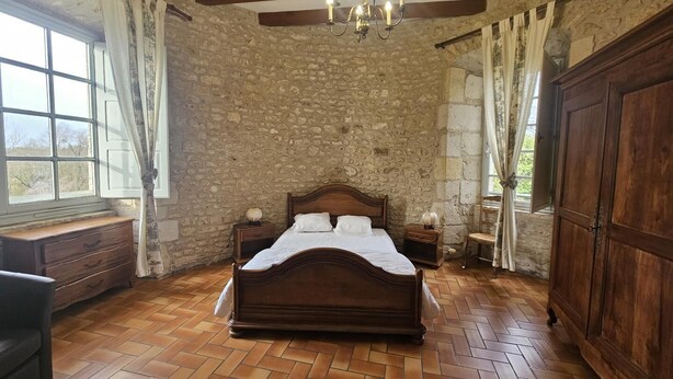 A bedroom with a wooden bed, stone walls, a chandelier, and a large window.