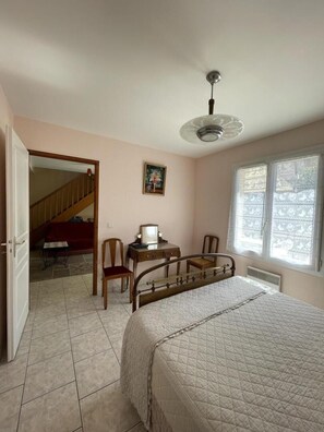 Quarto com cama, escrivaninha, cadeira, ventoinha no teto e janela.