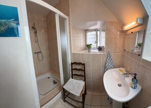 A bathroom with a shower, a sink, a chair, and a window.