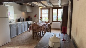 A kitchen with a dining area, featuring a tiled floor, wooden cabinets, a table set for dining, and a window with a view.