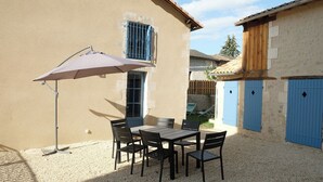 Un patio con una mesa y sillas, una puerta azul y un edificio color beige.