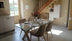 Un comedor con mesa de vidrio, sillas y un jarrón de flores.