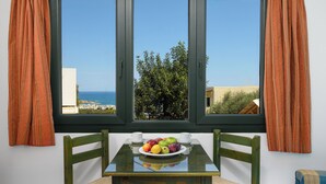 Una habitación con una mesa dispuesta para dos, un frutero y vista al mar a través de un ventanal grande.