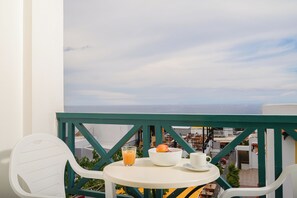A balcony with a white table, a white chair, a bowl of fruit, a glass of orange juice, and a cup. - Elen-Mari (Hersonissos)