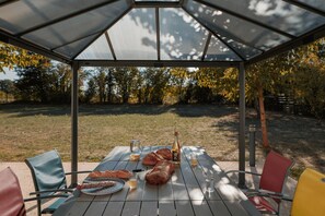 A covered outdoor dining area with a table set for a meal, chairs, and a view of the surrounding trees. - La Charmille - Saint-gaudent (SAINT-GAUDENT)