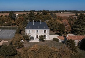 Une grande maison à deux étages, dotée d’une façade symétrique, entourée d’une pelouse bien entretenue et d’arbres majestueux.