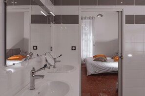 A modern bathroom with a large mirror, two sinks, a shower, and a bed with orange pillows. - La Charmille - Saint-gaudent (SAINT-GAUDENT)