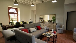 Een woonkamer met een bank, fauteuils, een salontafel en een eethoek met stoelen en een tafel.